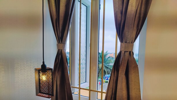 A room with a bed, a window with curtains, and a hanging lantern. - Nova Grande' (Hosur)