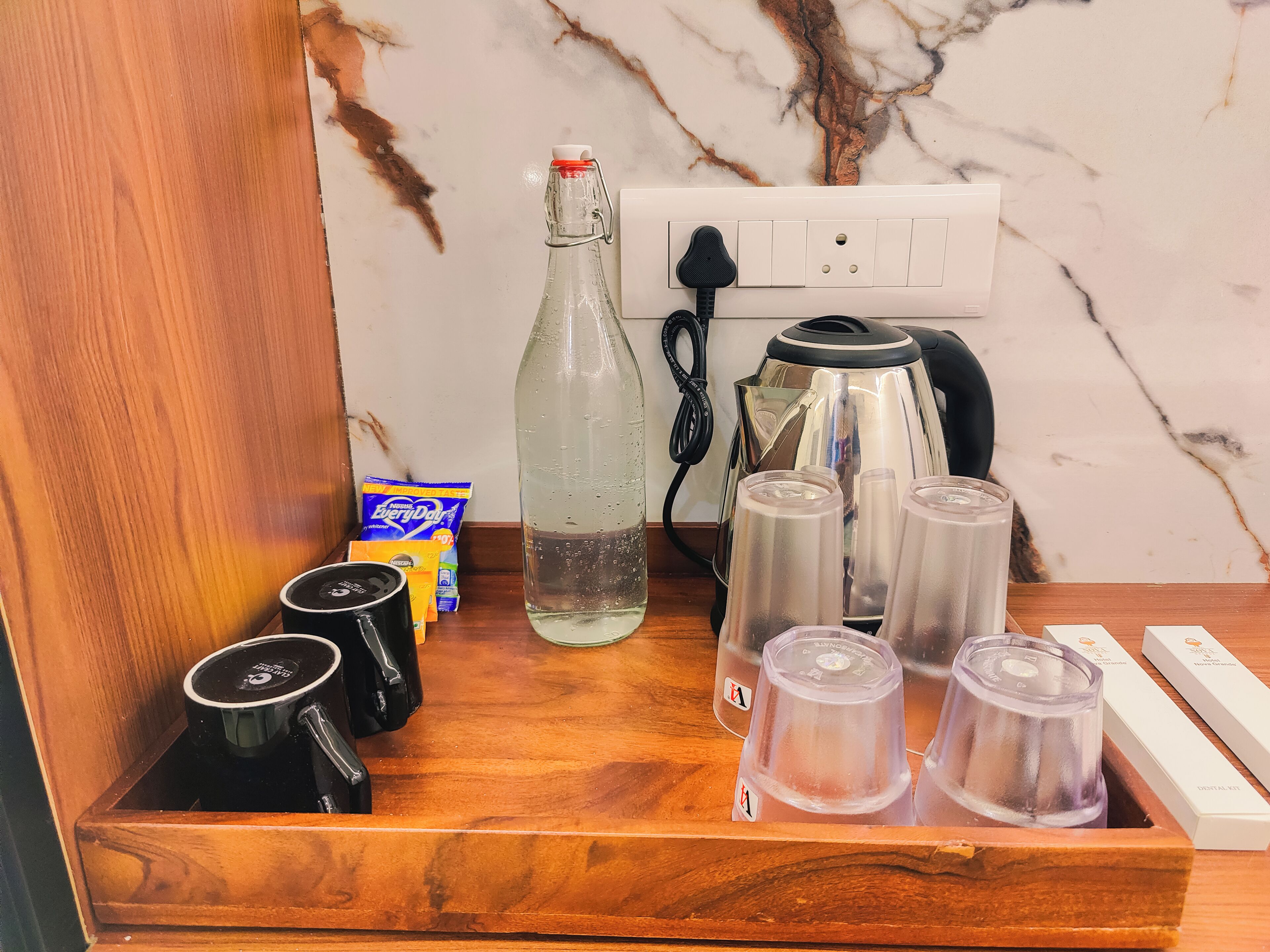 Una bandeja de madera con una botella de agua, una tetera, una caja de bolsitas de té y varias tazas.