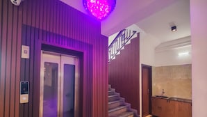 An elevator with a control panel, a staircase with a metal railing, and a kitchen area with a sink. - Nova Grande' (Hosur)