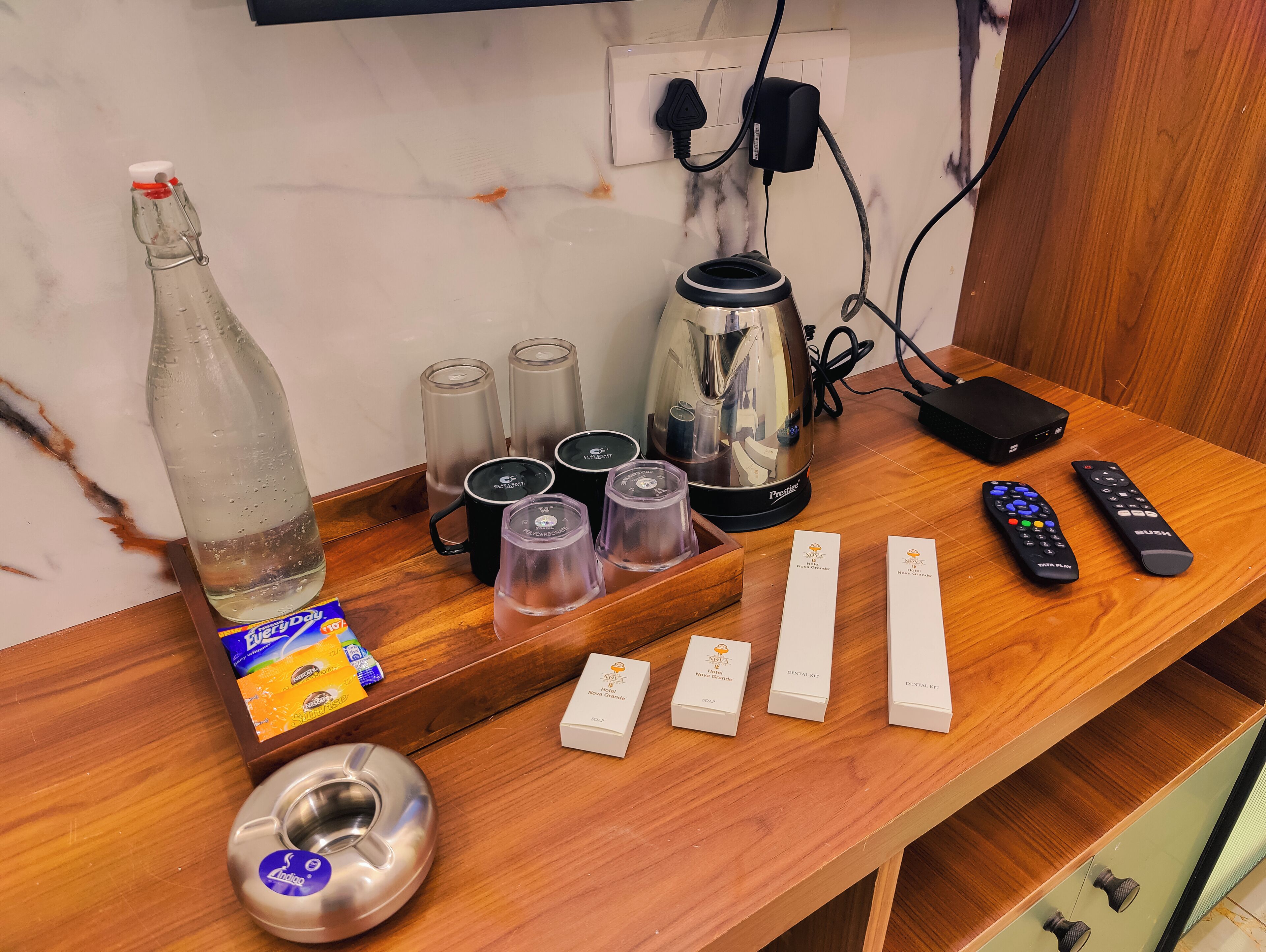 Une table en bois avec une bouteille, des verres, une bouilloire, des télécommandes et un narguilé.