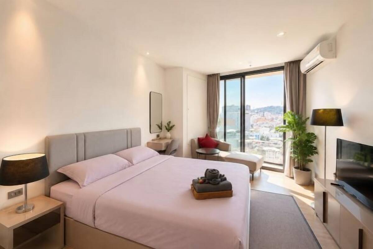 Une chambre d’hôtel équipée d’un lit, d’une table de chevet, d’une lampe, d’une télévision et d’une grande fenêtre donnant sur la ville.