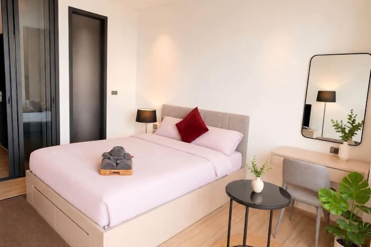 Une chambre à coucher avec un lit, une table de chevet, une lampe, un miroir et une petite plante en pot.