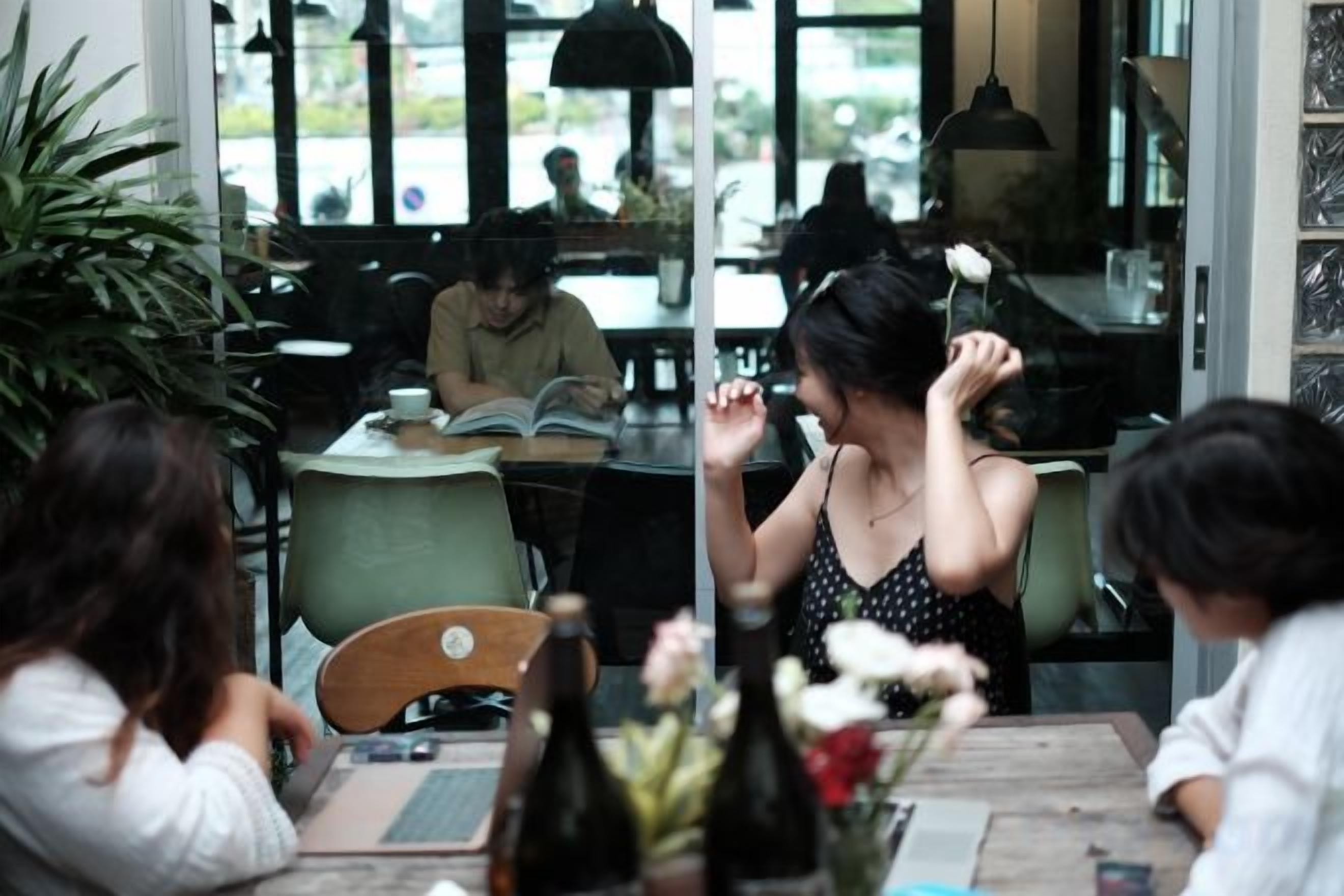 A cafe with tables and chairs, a person reading a book, and another person with a laptop.