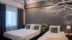 Une chambre d’hôtel avec deux lits, une grande fresque représentant un arbre sur le mur, une plante et une lampe.
