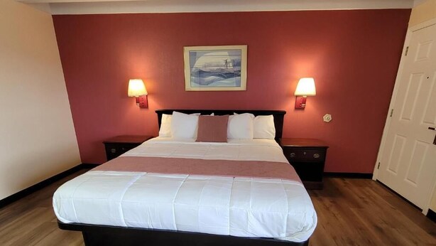 Quarto de hotel com uma cama grande, duas mesas de cabeceira, um quadro na parede e uma porta.