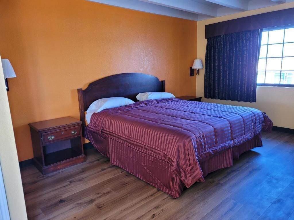 A bedroom with a wooden bed, a nightstand, and a window with curtains.
