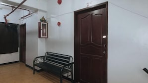 A hallway with a wooden door, a bench, and a framed picture on the wall. - MCP Transient near NAIA (Pasay)