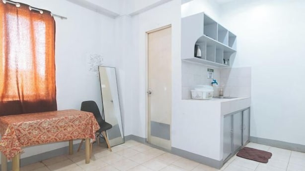 A small, clean room with a table, a chair, a mirror, a cabinet with shelves, and a door. - MCP Transient near NAIA (Pasay)