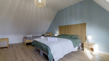 Un dormitorio con techo inclinado, una cama con ropa de cama verde, una mesita de noche con lámpara y un cabecero de madera.