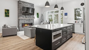 A modern kitchen with a large island, a stone fireplace, and pendant lighting. - New 4 bed/3 bath, one level home - private hot tub, BBQ, garage & office (Silver Star Mountain)