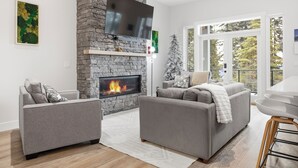 A modern living room with a stone fireplace, grey sofas, and a flat-screen TV. - New 4 bed/3 bath, one level home - private hot tub, BBQ, garage & office (Silver Star Mountain)