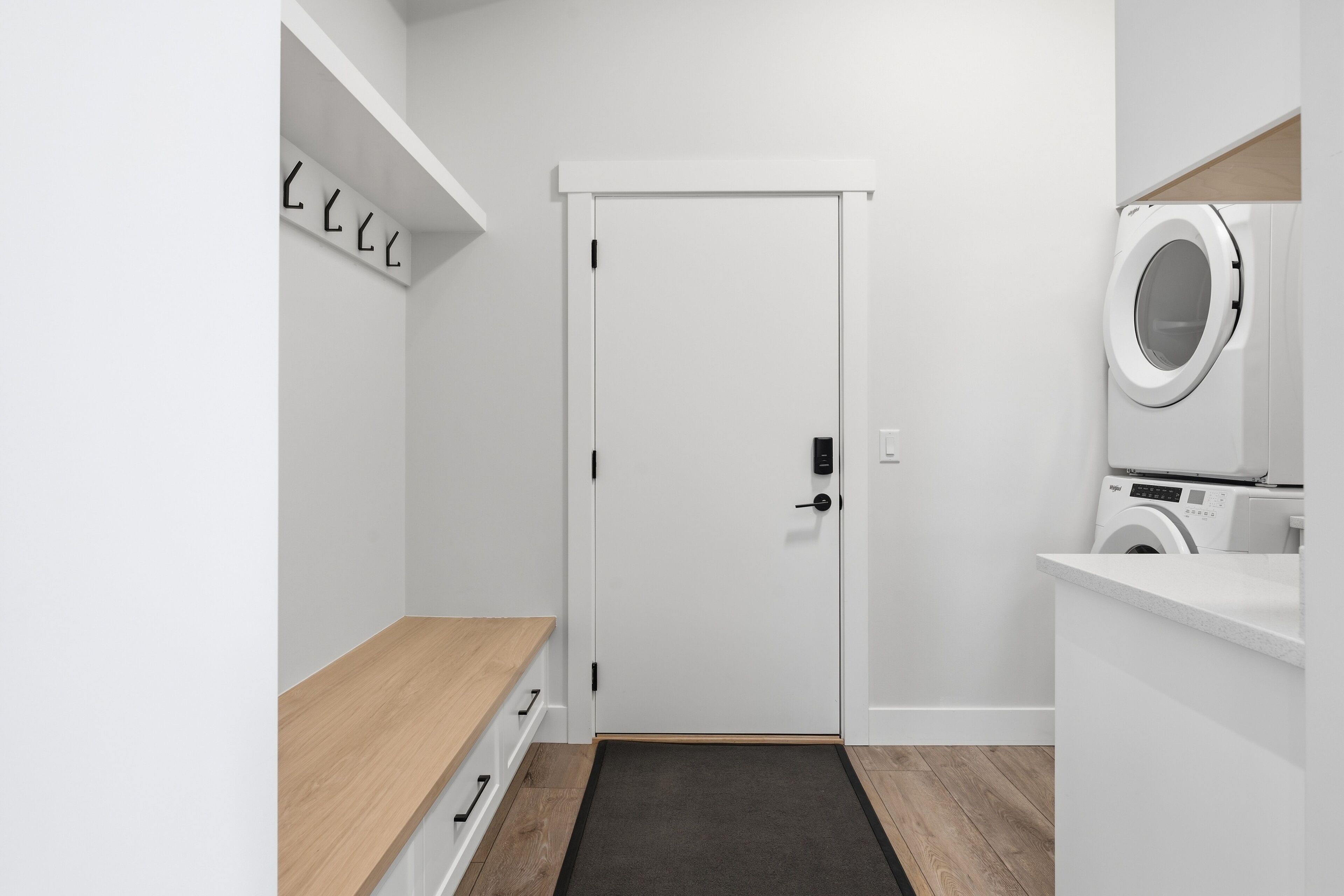 A laundry room with a door, a washing machine, and a wooden bench.