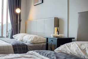 Een hotelkamer met twee bedden, een nachtkastje met een lamp en een raam met gordijnen.