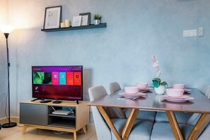 Een moderne woonkamer met een flatscreen televisie, een eettafel met roze kommen en een bank.