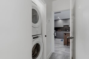 A laundry room with stacked washing machines and a modern kitchen in the background.