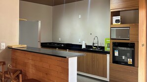 A modern kitchen with a wooden island, bar stools, a built-in oven, and a microwave. - Casamares beach in Ipioca, Maceió, Angra de Ipioca condominium, Hibiscus Beach Club (Maceió)