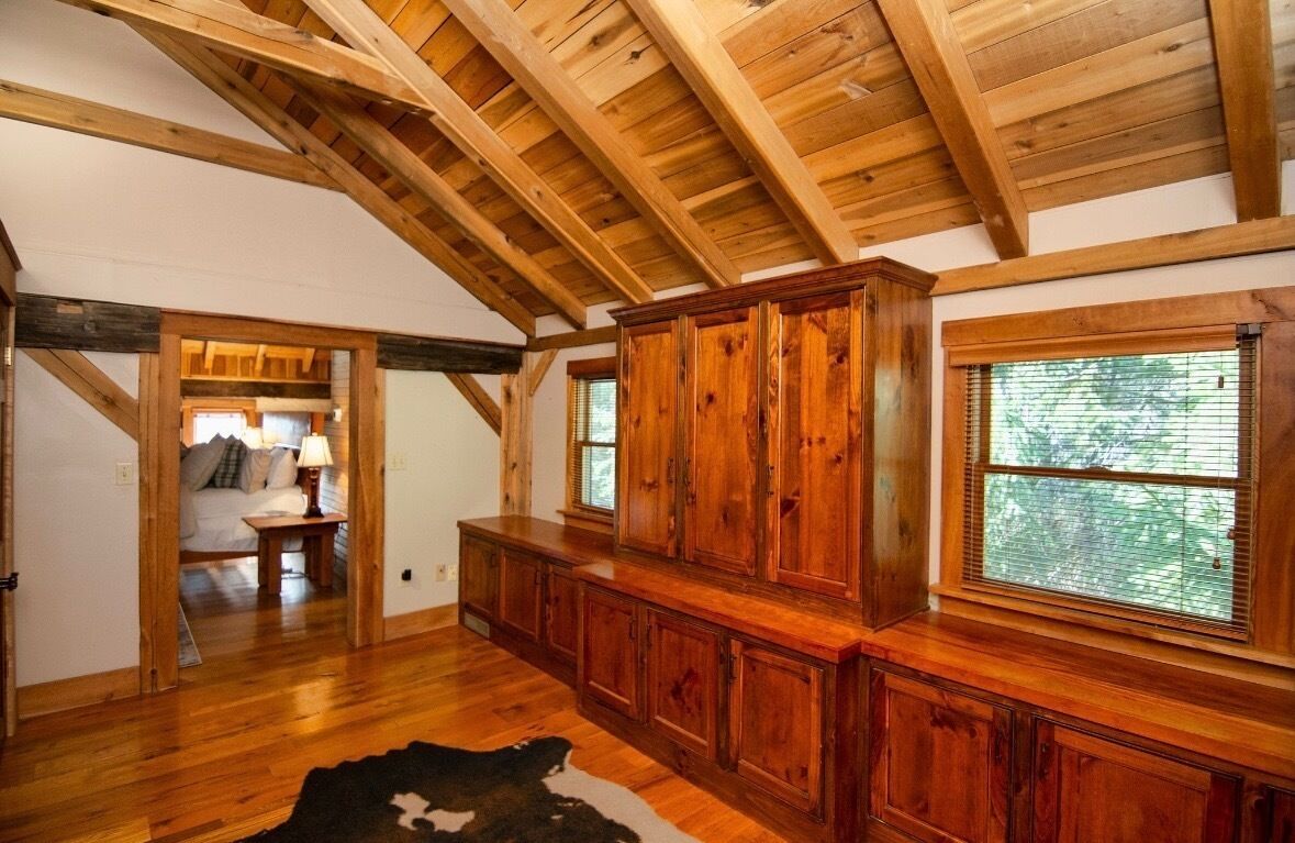 Une pièce spacieuse avec des poutres apparentes, une grande armoire en bois et une fenêtre équipée de stores.