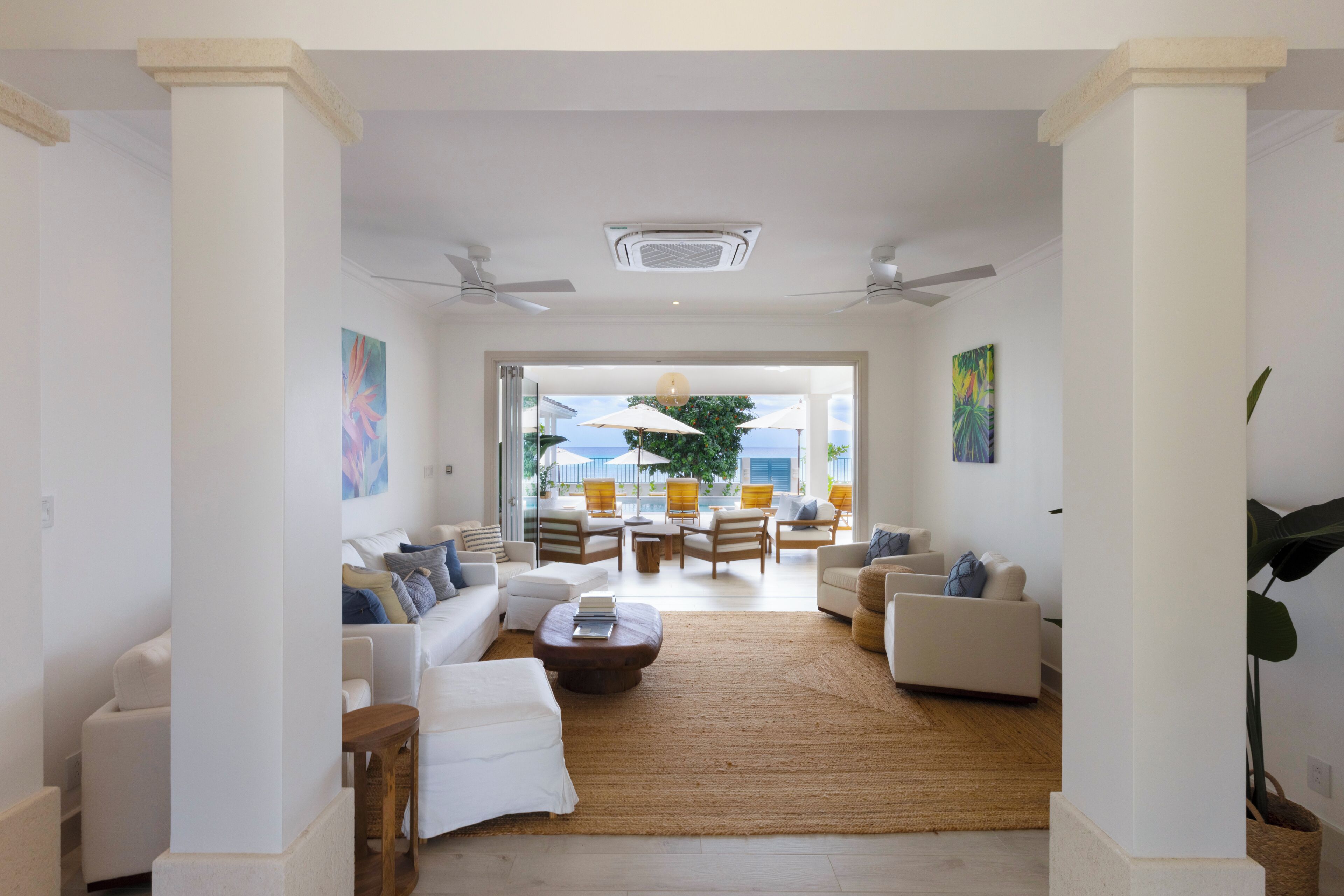 A spacious living area with a large rug, white sofas, and a view of the outdoors through a glass door.
