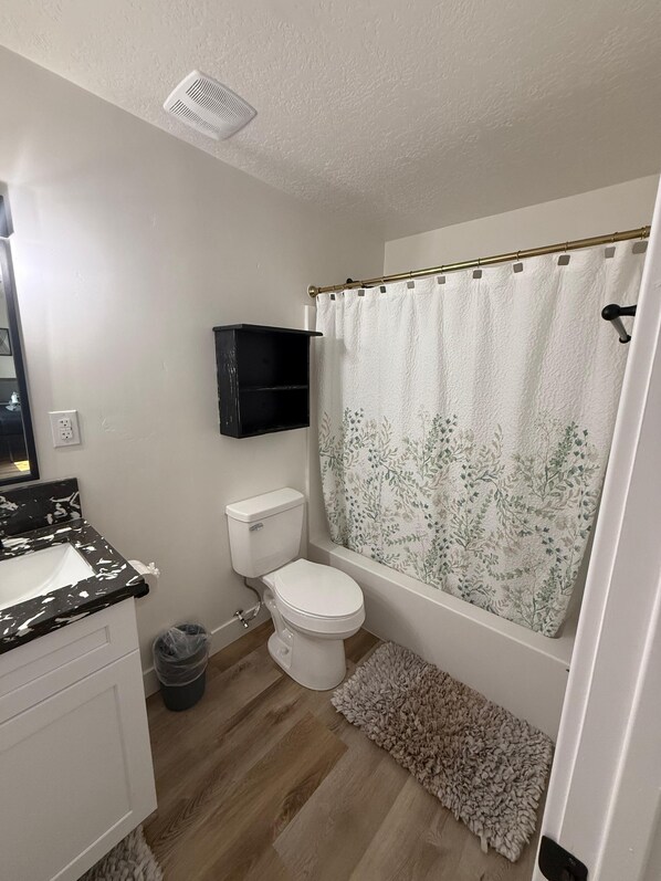 Un baño con inodoro, lavamanos, cortina de ducha y un pequeño estante.