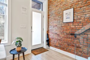 Une piÚce avec un mur en briques, une porte, une petite table avec une plante et un tableau encadré accroché au mur.