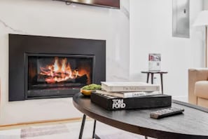 Un salon moderne avec une cheminée, une pile de livres, une télécommande et une petite table.