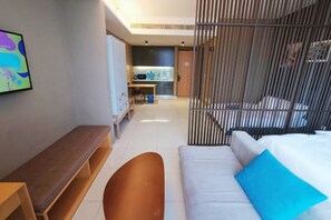 Una habitación de hotel moderna con una cama, un banco, un escritorio y una kitchenette al fondo.