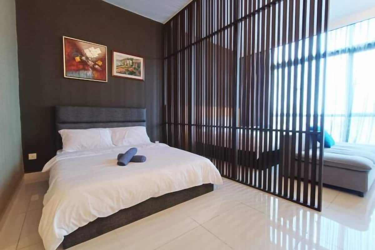 Een moderne hotelkamer met een groot bed, een donker hoofdeinde en uitzicht door een scheidingswand.