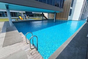 Ein moderner Poolbereich mit klarem, blauem Wasser, Holzterrasse und Metallleiter.