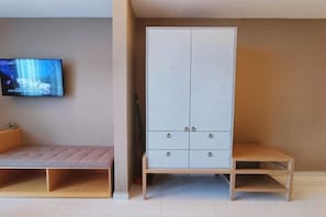 Een kamer met een aan de muur bevestigde televisie, een garderobe met twee deuren en een bankje.