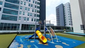 Un parque infantil con un tobogán amarillo y estructuras para escalar, rodeado de edificios modernos.