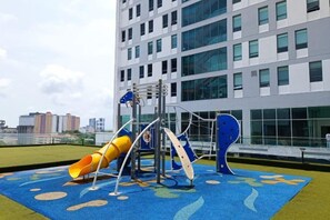 Ein Spielplatz mit Rutsche und Klettergerüsten vor einem modernen Gebäude mit großen Fenstern.