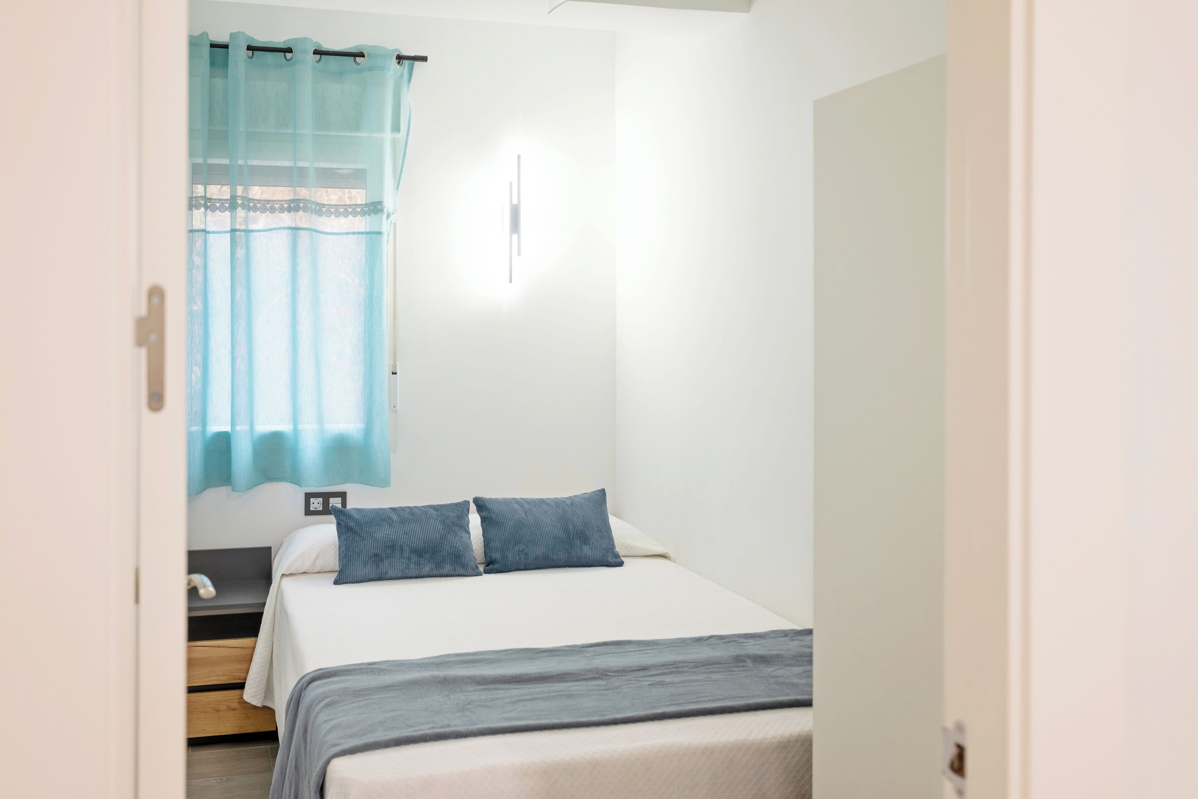 Une chambre à coucher avec un lit, une table de chevet et une fenêtre avec un rideau.