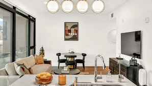 Una sala de estar moderna con un sofá, un comedor, una isla de cocina con pileta y un televisor montado en la pared.