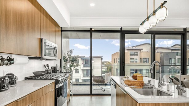 Una cocina moderna con armarios de madera, cocina a gas y un amplio ventanal con vistas a un paisaje urbano.