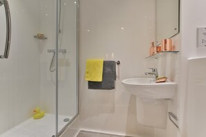 A modern bathroom with a glass shower enclosure, a white sink with a copper faucet, and a yellow towel on the wall. - Student Only Willowbank (Glasgow)