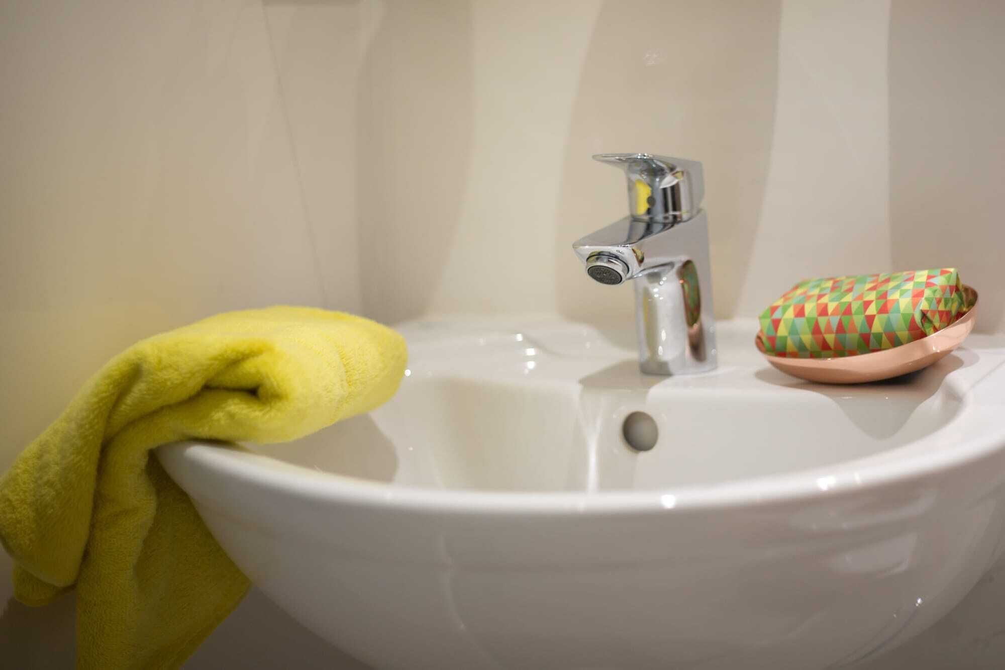 A bathroom sink with a yellow towel and a colorful soap dish.