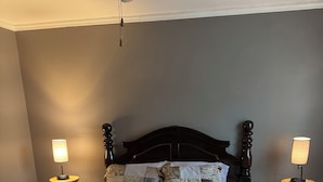 Un dormitorio con una cama de madera oscura, una colcha acolchada, dos lámparas de noche y un ventilador de techo.