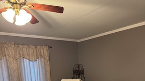 Una sala de estar con un sillón beige, una mecedora marrón, un pequeño reposapiés, un televisor y un ventilador de techo.