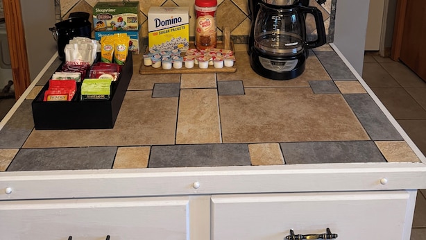 Una encimera de cocina con una cafetera, una caja de sobres de azúcar Domino y varios alimentos.