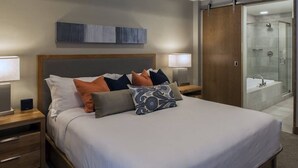A modern hotel room with a large bed, bedside lamps, a wooden nightstand, a bathroom with a glass shower, and a wooden wardrobe. - Luxury 1-Bedroom Condo at Grand Colorado on Peak 8 — Ski-In/Ski-Out! (Breckenridge)