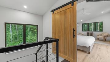 Une chambre moderne dotée d’une grande porte coulissante, d’un lit, d’une chaise et offrant une vue sur une forêt grâce à de grandes fenêtres.