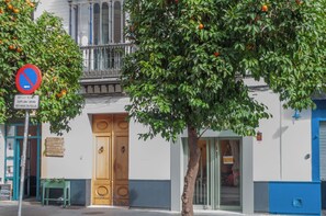 A building with a wooden door, a balcony, and a tree with oranges. - NEW Luxurious Epicenter III Apartment: Free parking, Top location,Free A/C&Wi-Fi (Sevilla)
