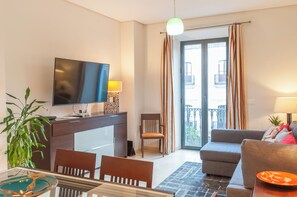 Una sala de estar moderna con un televisor de pantalla plana, una mesa de comedor con sillas, un sofá y un balcón con cortinas.