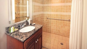 Un bagno con piano in granito, lavabo bianco, specchio e doccia con piastrelle color beige.