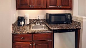 Cucina compatta con mobili in legno, piano di lavoro in granito, macchina del caffè, lavello, forno a microonde ed elettrodomestici.