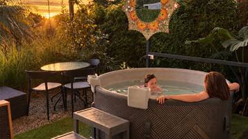 Un bain à remous où se trouvent une personne et un enfant, entouré d’un jardin agrémenté d’un miroir décoratif et d’une table avec des chaises.