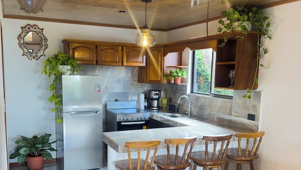 Une cuisine avec des meubles de rangement en bois, un réfrigérateur, une cuisinière et des tabourets de bar.