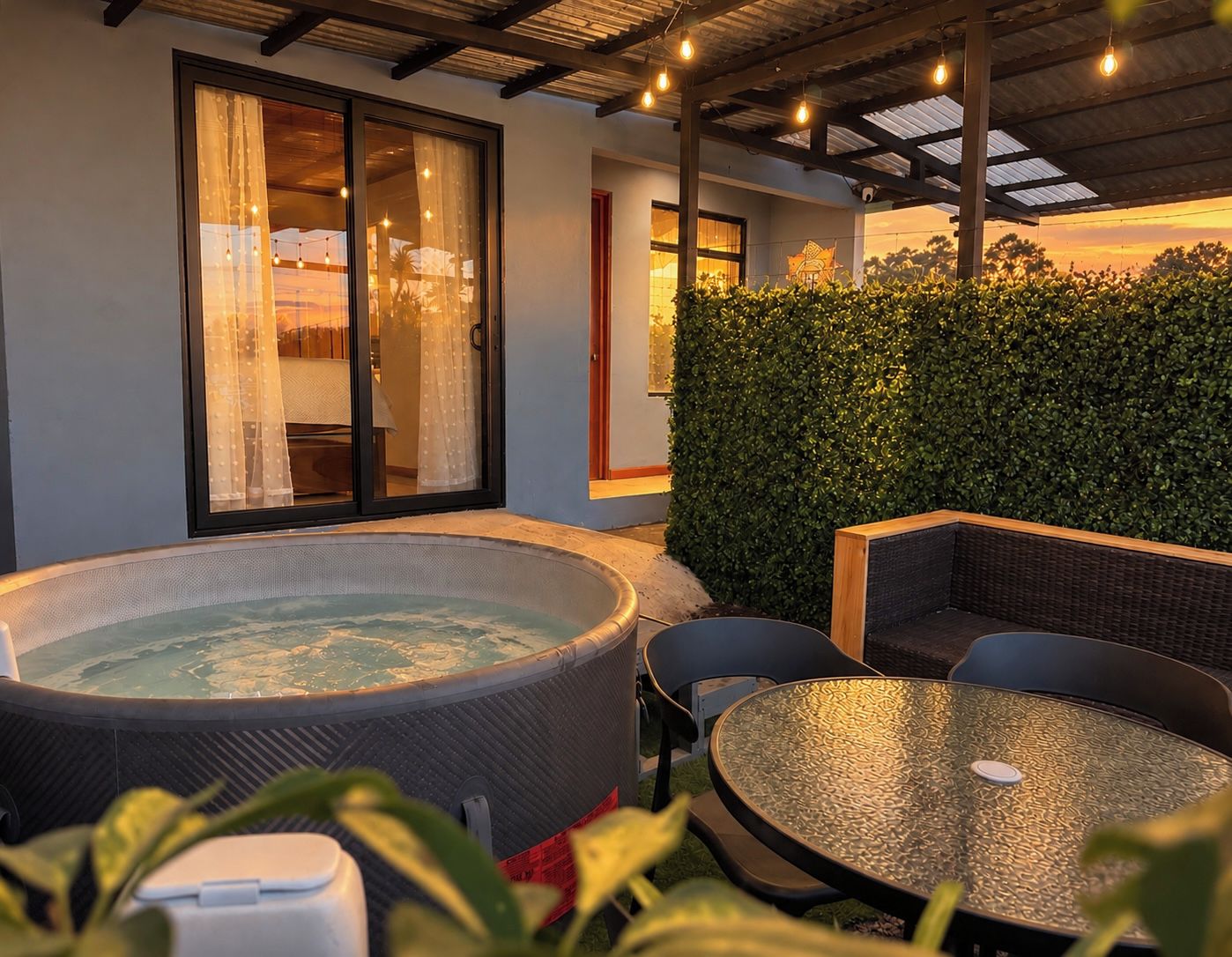A hot tub with a view of a landscape, a round table, and a seating area with a hedge in the background.