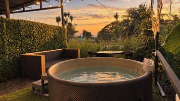 An outdoor hot tub area with seating, surrounded by greenery and a view of the sunset.