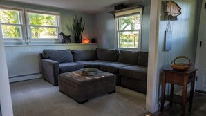 A cozy living room with a sectional sofa, a small ottoman, and a wooden side table. - 8 Acre Lower-Level Hobby Farm Getaway (Prior Lake)